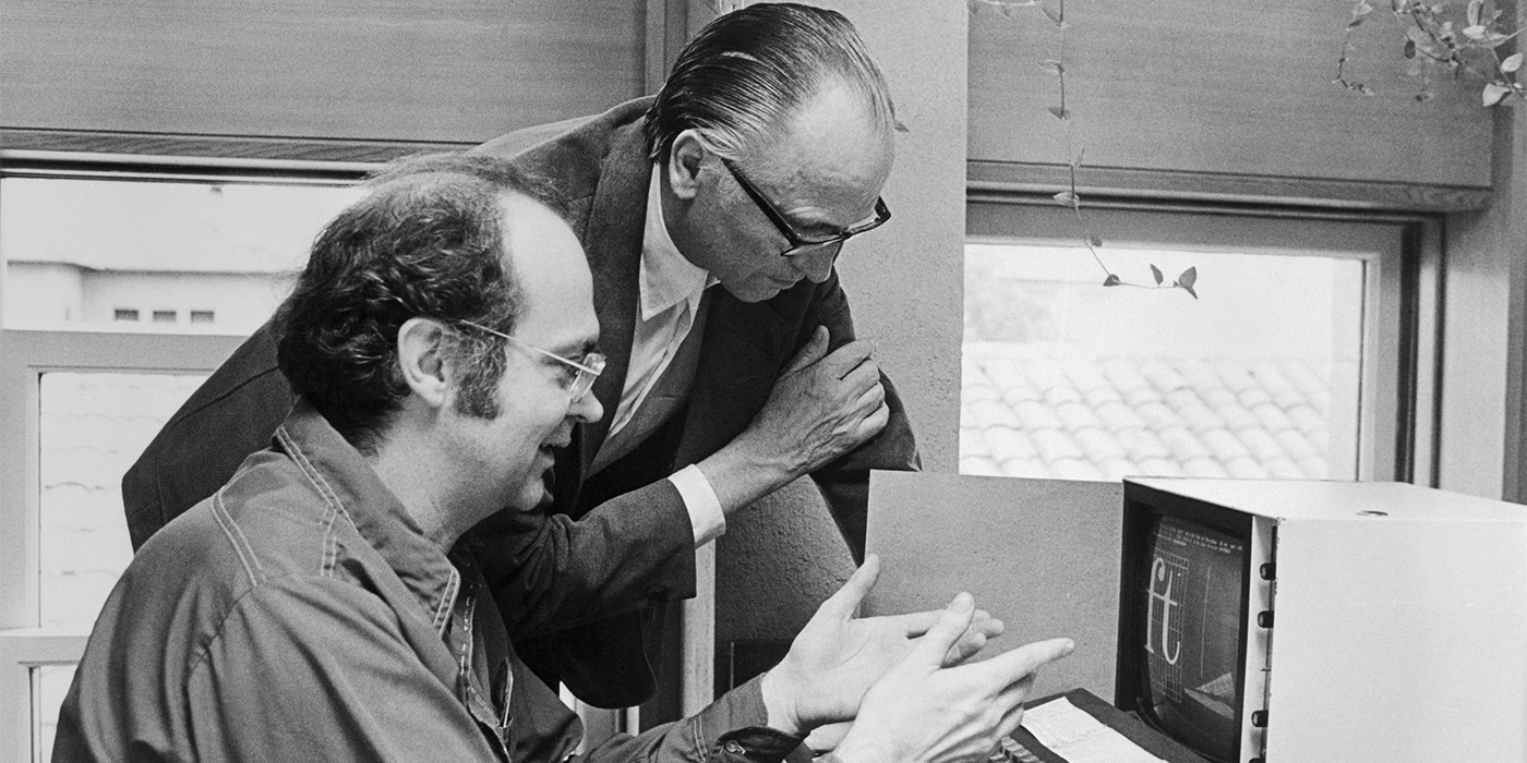 Computer scientist Don Knuth and type designer Hermann Zapf looking over font proofs displayed on a computer.